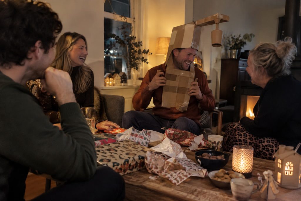 Familie lacht op pakjesavond rond een salontafel vol open cadeaupapier en een zelfgemaakte surprise